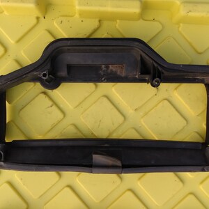 Puede incluir: Marco de plástico negro con una abertura rectangular. El marco tiene una superficie texturizada y parece ser utilizado para una pieza de automóvil.