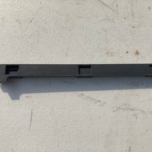Può includere: Un pezzo di rivestimento in plastica nera con tre aperture rettangolari. Il pezzo di rivestimento ha la scritta "12278585" stampata su di esso.