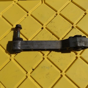 Könnte beinhalten: Ein silbernes Autoteil aus Metall mit einer schwarzen Gummibüchse an jedem Ende. Das Teil hat an einem Ende eine Gewindeschraube.