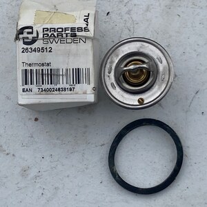 Peut inclure: Un thermostat de voiture argenté avec un joint en caoutchouc noir. Le thermostat a une valve en laiton et est étiqueté "26349512". L'emballage est étiqueté "PROFESS PARTS SWEDEN" et "Thermostat". Le code EAN est 7340024638197.