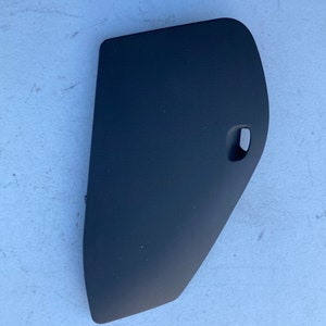 Puede incluir: Pieza de coche de plástico negro con forma curva y una pequeña abertura en el lateral.