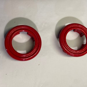 Puede incluir: Dos anillos de plástico rojo con un diseño de círculos concéntricos. Los anillos tienen un agujero en el centro.