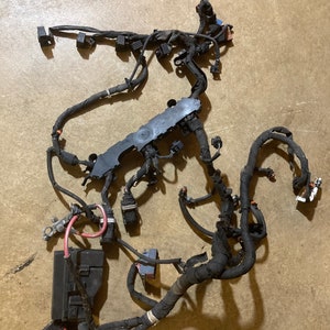 Könnte beinhalten: Ein schwarzer Kfz-Kabelbaum mit mehreren Steckverbindern und einer schwarzen Box. Der Kabelbaum liegt auf einer braunen Oberfläche.