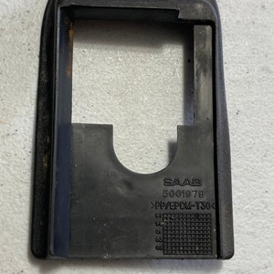 Puede incluir: Pieza de coche de plástico negro con el texto "SAAB 5001979 >PP/EPDM-T30<" impreso en ella.