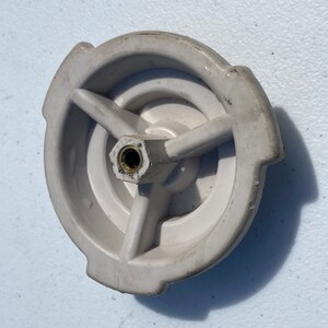 Puede incluir: Pomo de plástico blanco con un diseño de tres puntas y un tornillo de latón en el centro.