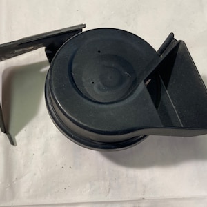 Könnte beinhalten: Eine schwarze Kunststoff-Hupe mit einem runden Lautsprecher und einem gebogenen Horn. Die Hupe ist an einer Metallhalterung befestigt.