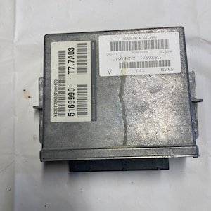 May include: A grey automotive control unit with a black label that reads "SAAB T7.7" and a white label with the text "YS3DF78K637009109 5169990 T7.7A03".