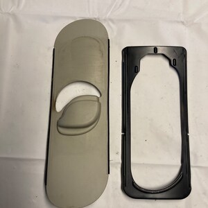 以下が含まれることがあります： 黒のトリムと黒のプラスチックフレームが付いたベージュのプラスチック製の自動車部品。フレームは角が丸みを帯びた長方形です。