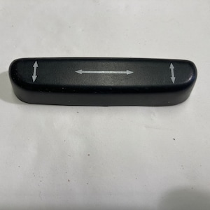 May include: Black plastic lever with arrows indicating up and down directions. The lever is used to adjust the height of a chair or seat.