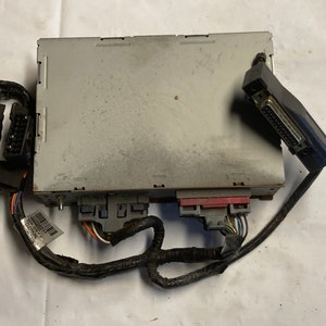 May include: A gray electronic control unit with multiple black wires and connectors. The unit has a serial number label and a red and gray connector on the front.