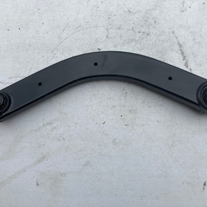 Op de afbeelding: Zwarte metalen auto-ophanging arm met twee ronde gaten aan elk uiteinde.