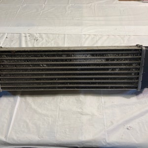 May include: A silver intercooler with black end caps. The intercooler has a rectangular shape and is made of metal with a grid pattern.
