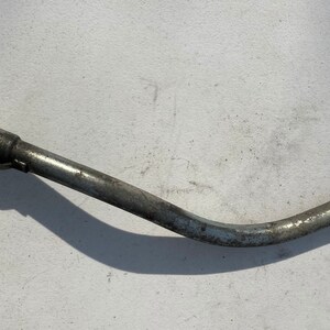 Peut inclure: Un goulot de remplissage de carburant incurvé en métal argenté, avec un crochet et un joint en caoutchouc. Le tube métallique présente une légère usure. Conception simple et fonctionnelle.