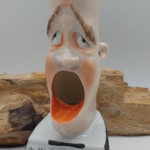 Może przedstawiać: Ceramiczna figurka łysiejącego mężczyzny z szeroko otwartymi ustami, pomalowana w odcieniach brzoskwini i brązu. Podstawa jest biała z napisem "by the light of the silvery Moon". Obecna jest również nuta muzyczna.