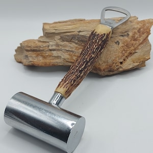 May include: A bottle opener and meat tenderizer combination tool. The handle is made of brown antler material, and the head is a shiny silver metal. The bottle opener is made of stainless steel. The tool is designed for kitchen use.