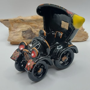 Pode incluir: Estatueta de carro vintage preto com detalhes em vermelho e amarelo. O carro tem um acabamento brilhante e apresenta detalhes intrincados nas rodas e na carroceria. O design do carro inclui um farol amarelo e padrões decorativos.