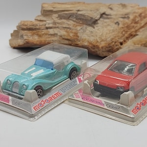 Può includere: Due modellini di auto in metallo in confezioni di plastica trasparente. Uno è una Morgan azzurra, l'altra una Renault Clio rossa. Entrambi sono su schede con il marchio "Majorette".