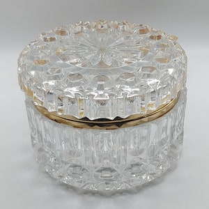 Puede incluir: Un tarro de cristal transparente y facetado con borde y tapa dorados. La tapa presenta un dise&ntilde;o central en forma de estrella. El tarro es redondo y se apoya sobre una superficie blanca. El cristal tiene un patr&oacute;n de diamante.