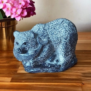Pode incluir: Estatueta de urso cinza escuro com textura detalhada e um peixe na boca. O urso é retratado em posição sentada. O objeto decorativo tem uma aparência ligeiramente envelhecida.