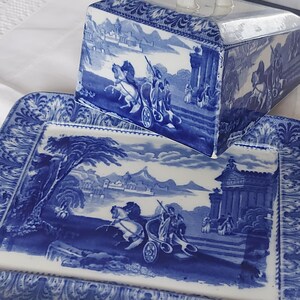 May include: Blue and white porcelain serving dish and lid with a classical scene. The rectangular dish and lid feature a detailed illustration of a chariot pulled by horses, set against a landscape with buildings and mountains. The edges have a decorative border.