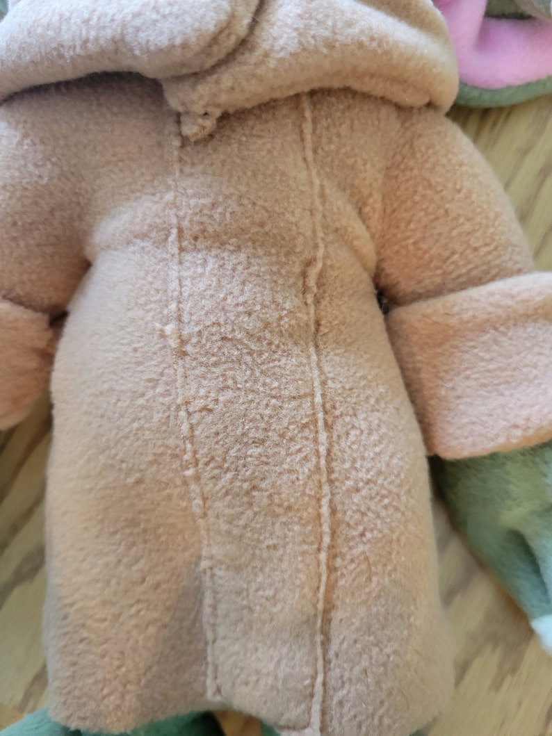 May include: A plush toy with a brown hooded jacket and green and pink accents. The jacket has a seam down the front.
