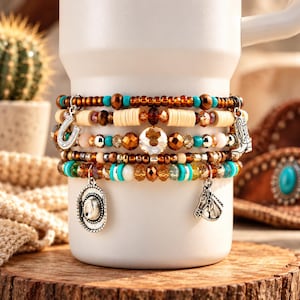 Puede incluir: Una pulsera de varias hileras con cuentas de color marrón, turquesa y crema. La pulsera incluye dijes plateados con forma de herradura, bota de vaquero, sombrero de vaquero y cabeza de caballo, dispuestos en un diseño de capas.
