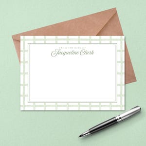 May include: A stationery set featuring a white notecard with a light green trellis design border and the text "From the Desk of Jacqueline Clark." Includes a brown envelope and a black and silver pen.