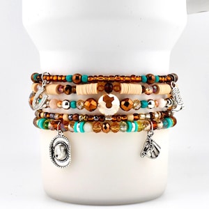 Può includere: Un bracciale a più fili con perline color marrone, turchese e crema. Il bracciale presenta ciondoli color argento a forma di ferro di cavallo, cappello da cowboy, stivale e testa di cavallo, intervallati da cristalli sfaccettati.