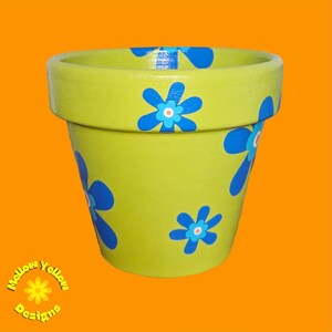 May include: A green terracotta flower pot with blue and white painted flowers. The pot is decorated with a simple floral design.