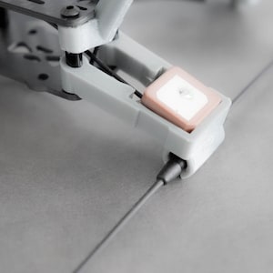 May include: Close-up of a gray drone with a small, square, white and pink antenna attached to the bottom.