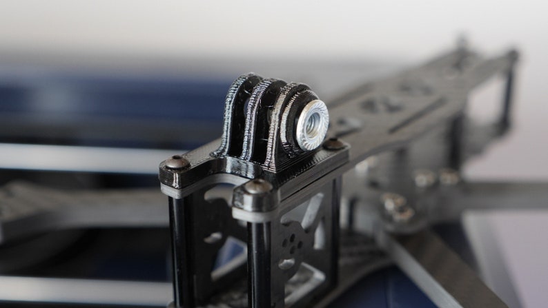 May include: Close-up of a black 3D printed GoPro mount with a silver threaded nut.