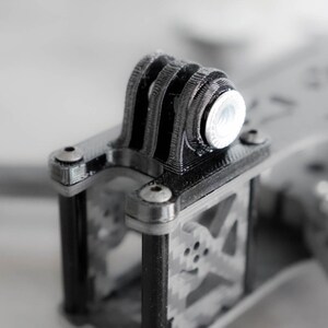 May include: Close-up of a black 3D printed drone frame with a silver GoPro mount.