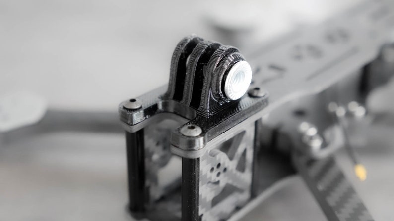 May include: Close-up of a black 3D printed drone frame with a silver GoPro mount.