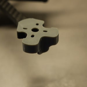 May include: A gray plastic 3D printed part with four holes in a star shape. The part is designed to be used as a mount for a motor or other component.