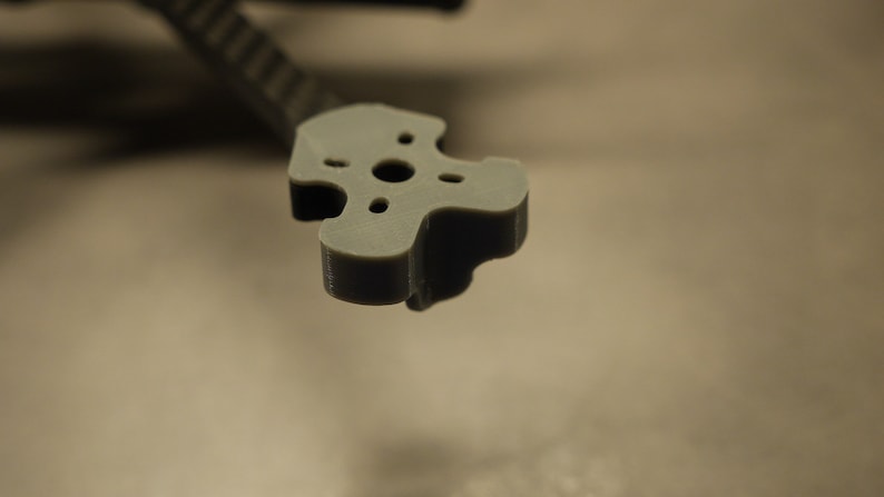 May include: A gray plastic 3D printed part with four holes in a star shape. The part is designed to be used as a mount for a motor or other component.