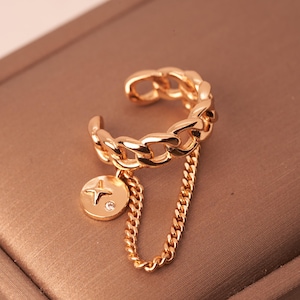 May include: A gold-toned ear cuff featuring a thick curb chain band. A delicate, thinner chain connects the main band to a small, round charm. The charm is embossed with a four-pointed star design and is accented with a single, tiny clear stone.