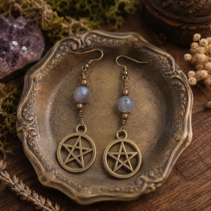 May include: A pair of dangle earrings featuring bronze-toned pentagram charms suspended from wire hooks. Each earring includes a single round, translucent grey stone bead accented by small bronze-colored metal spacers and coiled wire detailing.
