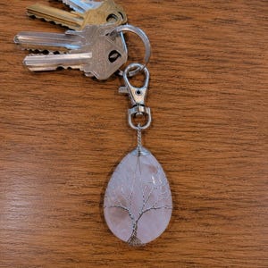 May include: A teardrop-shaped rose quartz pendant wrapped in silver-colored wire to resemble a tree, attached to a silver-tone metal lobster claw clasp and a split ring holding four assorted metal keys in silver and brass tones.