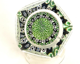 May include: A green, black and white glass paperweight with a multi-faceted design. The paperweight has a circular centre with a swirling pattern.
