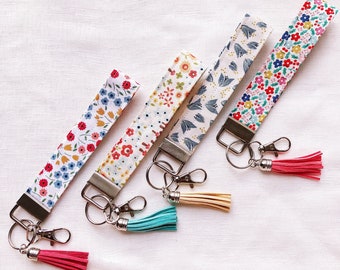 May include: Four colorful floral patterned keychains with silver key rings and tassels. The keychains are made of fabric and have a variety of floral patterns.