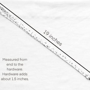 Op de afbeelding: Een wit stoffen koord met een klein zwart bloemenpatroon. Het koord meet 19 inch van het uiteinde tot de hardware, waarbij de metalen hardware ongeveer 1,5 inch toevoegt. De tekst luidt: 19 inches. Measured from end to the hardware. Hardware adds about 1.5 inches.