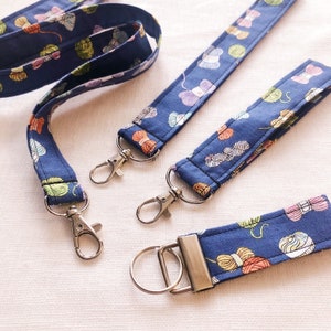 May include: Three blue keychains with silver key rings. Each keychain has a different length and features a blue fabric with a white and colourful yarn ball pattern.