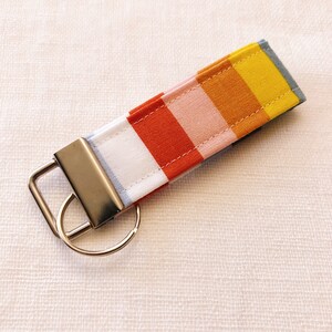 May include: A colorful striped key chain with a silver key ring. The stripes are yellow, orange, pink, red, white, and blue.