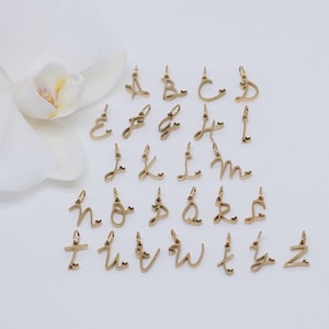 May include: A set of 26 gold-toned cursive letter charms with a small heart detail. The charms are arranged in alphabetical order on a white surface.