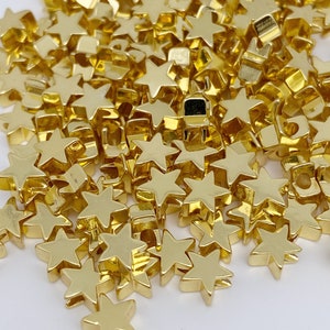 May include: A pile of gold-coloured star-shaped beads. The beads are small and have a smooth, shiny finish.