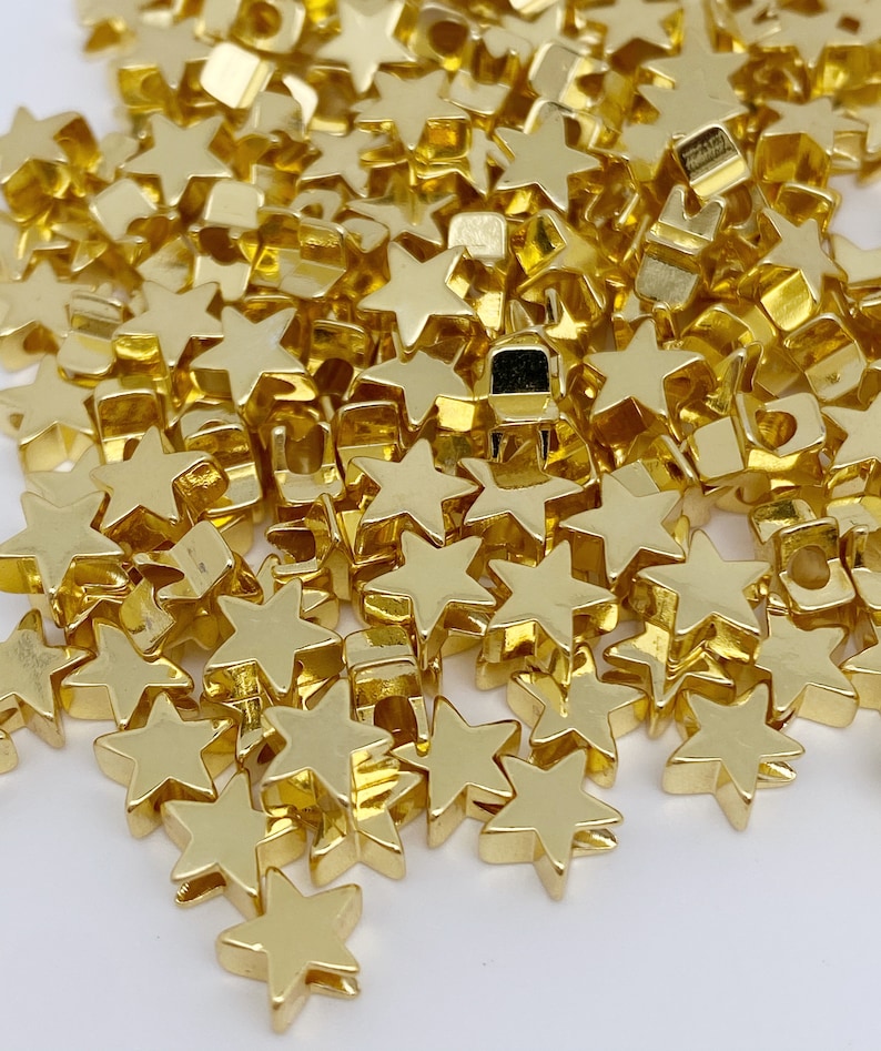 May include: A pile of gold-coloured star-shaped beads. The beads are small and have a smooth, shiny finish.