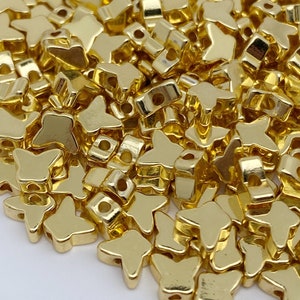 May include: A large pile of gold-coloured metal butterfly-shaped beads. The beads have a shiny, metallic finish.