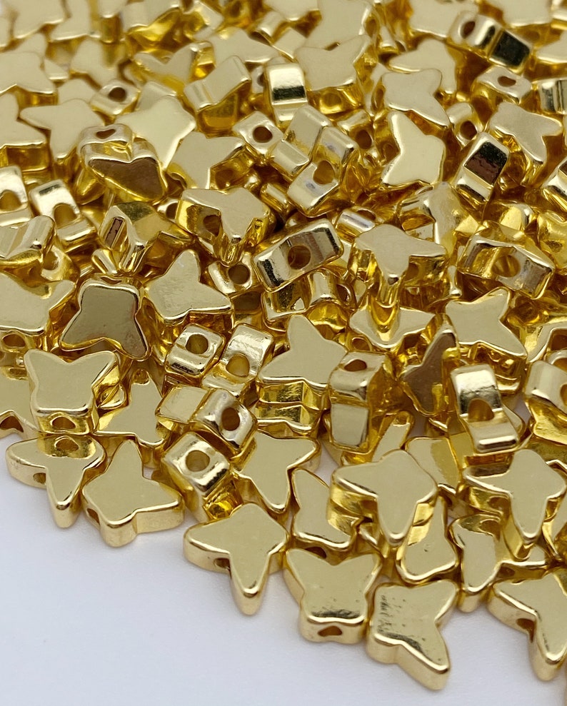 May include: A large pile of gold-coloured metal butterfly-shaped beads. The beads have a shiny, metallic finish.
