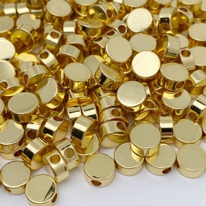 May include: A pile of gold-coloured metal beads with a hole in the centre of each bead. The beads are round and flat.