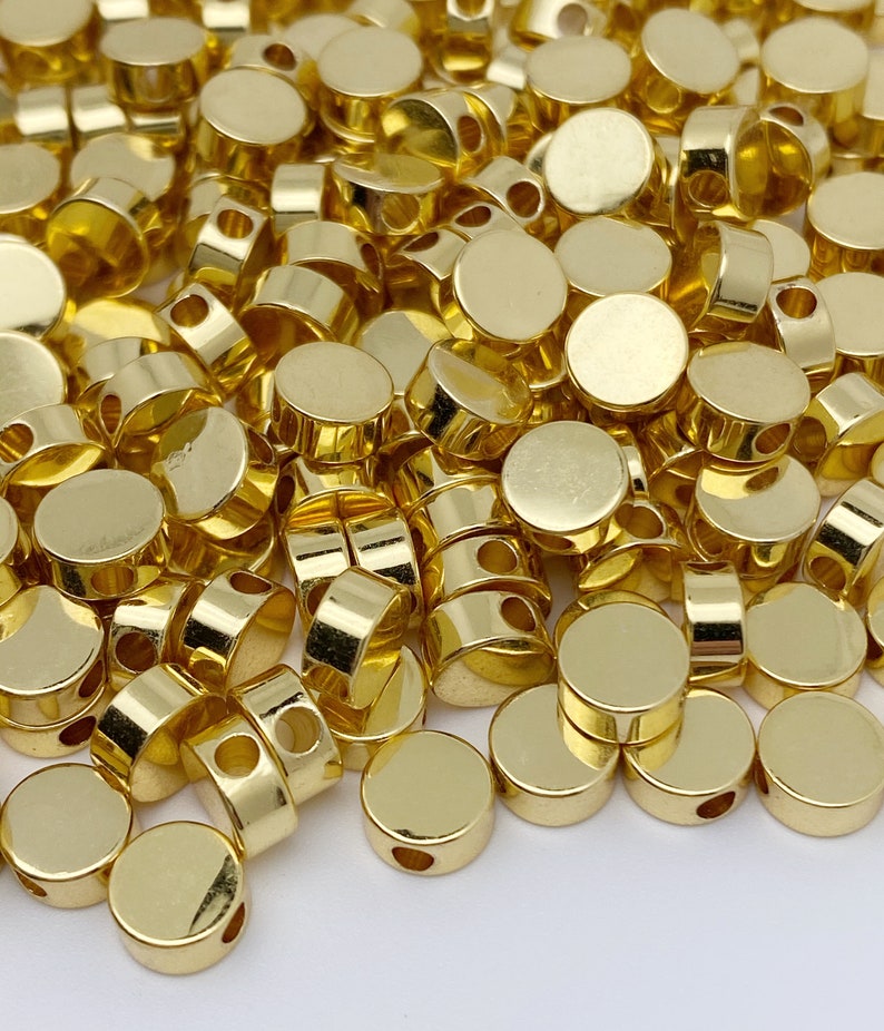 May include: A pile of gold-coloured metal beads with a hole in the centre of each bead. The beads are round and flat.